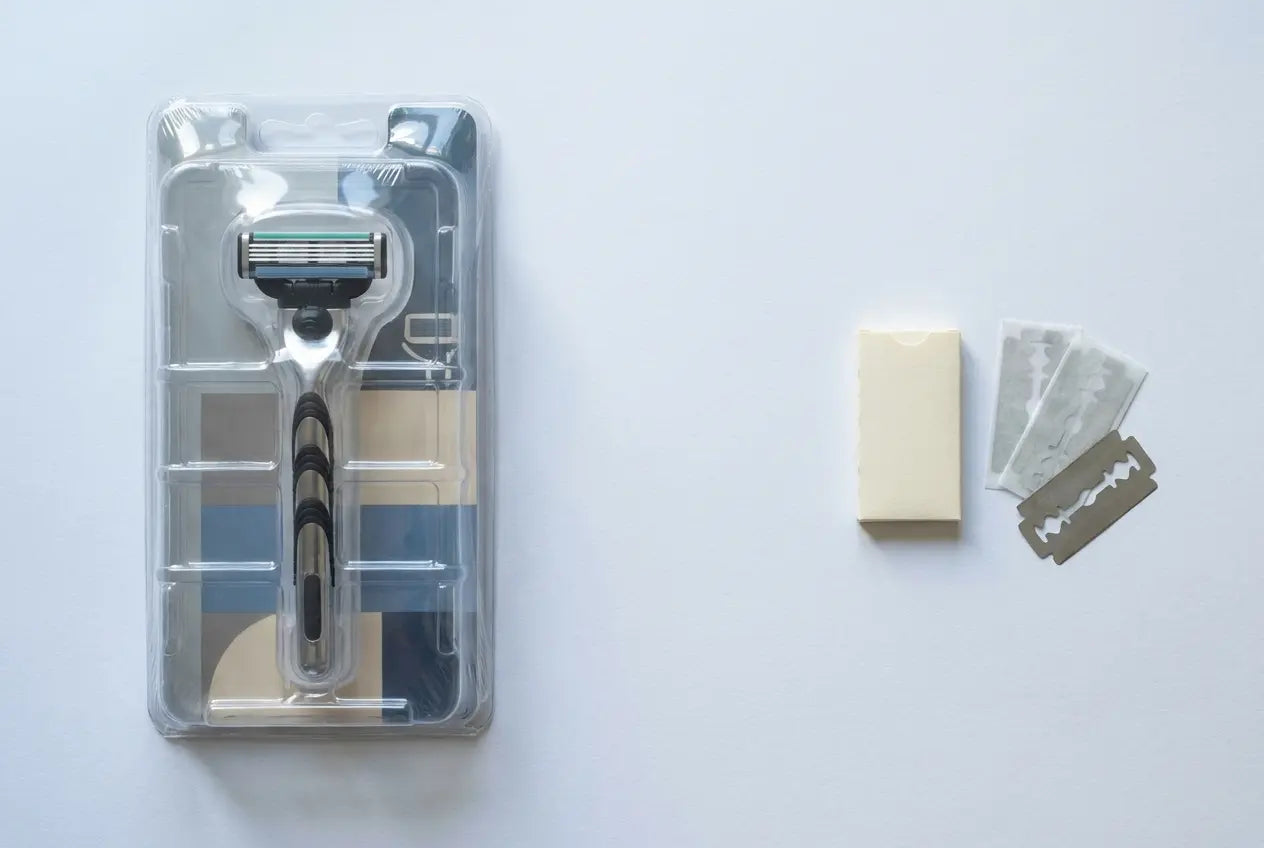 Blisterverpackung eines Klingenkopfs neben einem Papierumschlag mit DE-Klingen